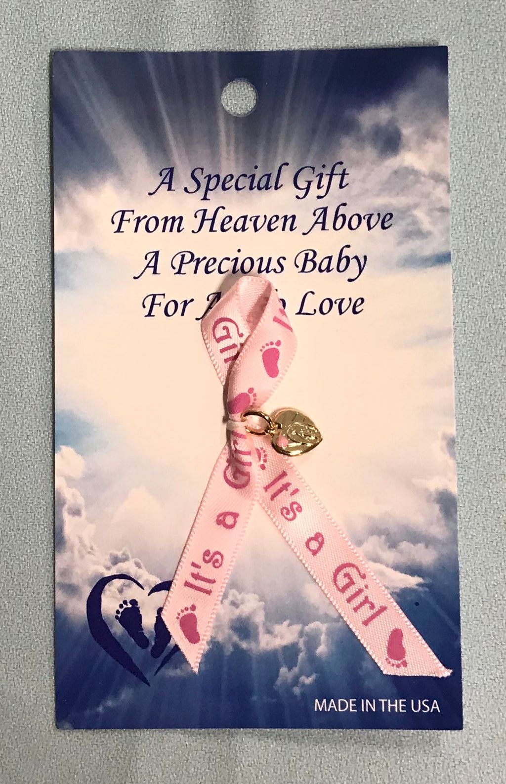 Pink ribbon says, "It's a Girl" with pink footprints. It has a gold colored Miraculous Medal inside a heart.